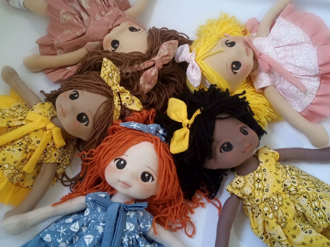 Cinco bonecas de diferentes etnias em um círculo, um boneca negra, uma ruiva, uma loira, uma morena e um branca.